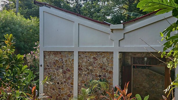 Un bâtiment doté d’une façade en pierre, d’un toit rouge et d’un jardin où poussent différentes espèces de plantes.