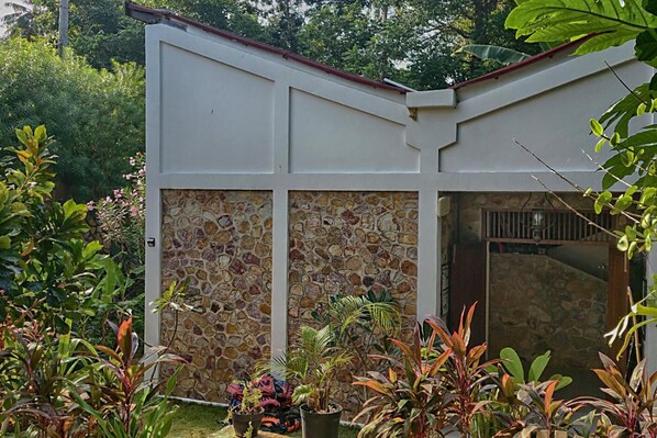 A building with a stone facade, a red roof, and a garden with various plants. - Ayu Hotel Karimunjawa (Karimun Jawa)