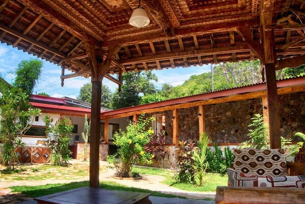 A covered outdoor area with a stone wall, wooden beams, and various plants. - Ayu Hotel Karimunjawa (Karimun Jawa)