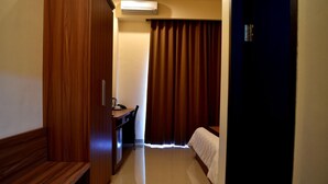 A hotel room with a wooden wardrobe, a desk with a chair, a bed, and a curtain. - Padadita Beach Hotel (Waingapu)