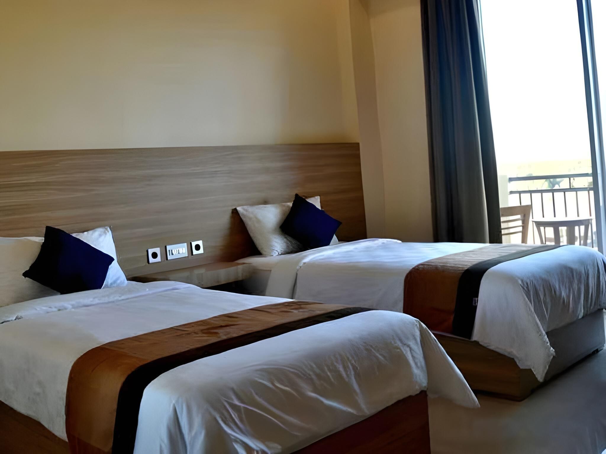 Une chambre d’hôtel avec deux lits, une tête de lit en bois, une vue sur le balcon et une fenêtre avec des rideaux.