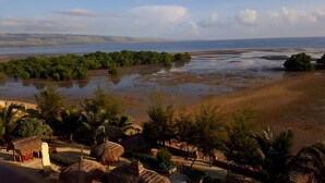 A coastal landscape with a beach, palm trees, and thatched-roof huts. - Padadita Beach Hotel (Waingapu)