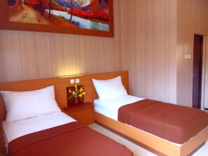 A hotel room with two single beds, wooden headboards, a nightstand with a vase of flowers, and a painting on the wall. - Hotel Kencana Rembang (Rembang)