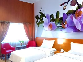 Habitación de hotel con dos camas, una silla roja, una mesita y una pared con un mural floral.