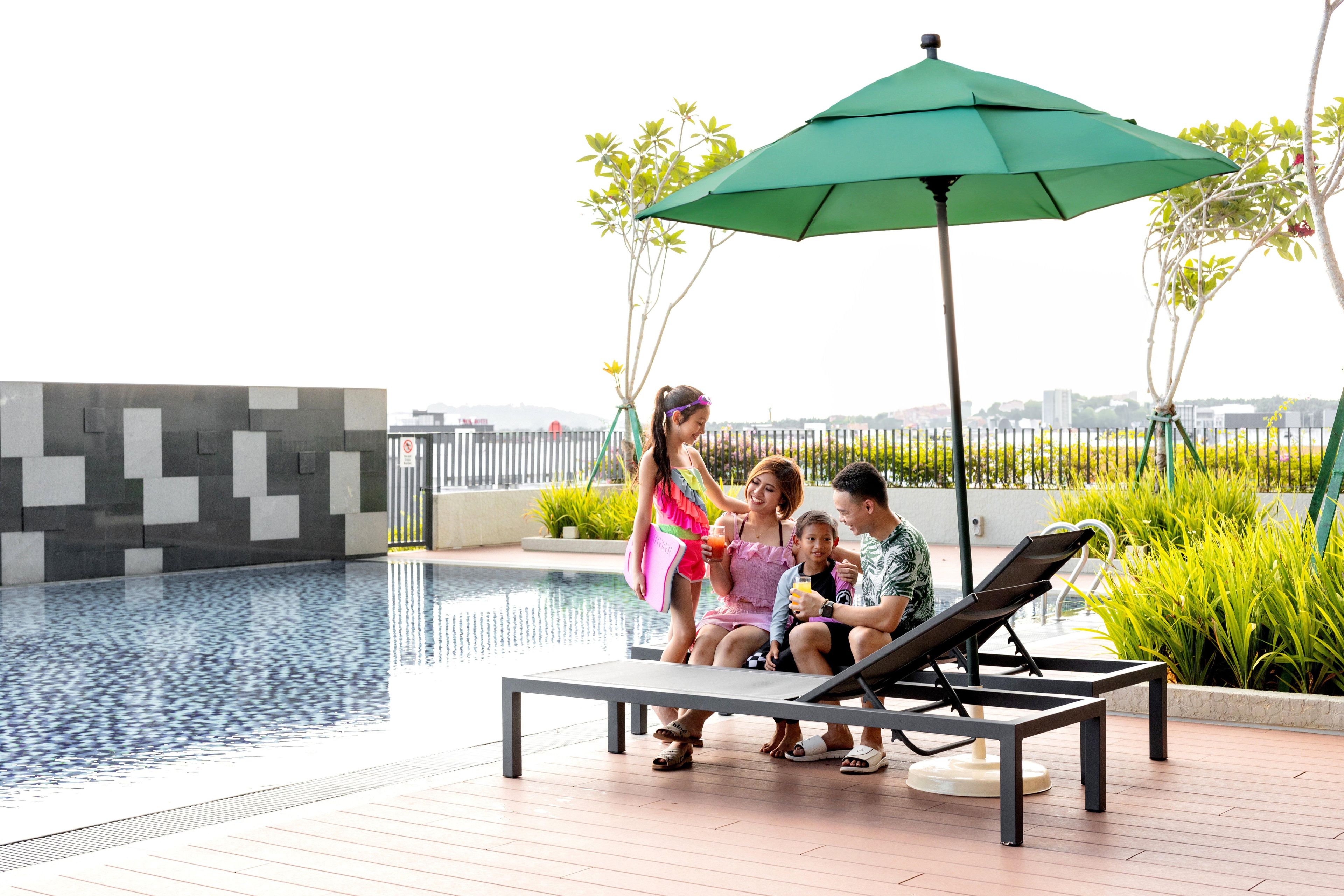 Un espace aménagé au bord de la piscine, avec des chaises longues et un parasol, entouré de verdure et offrant en arrière-plan une vue sur la ville.