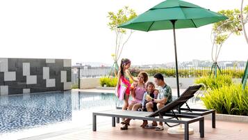 Un espace aménagé au bord de la piscine, avec des chaises longues et un parasol, entouré de verdure et offrant en arrière-plan une vue sur la ville.