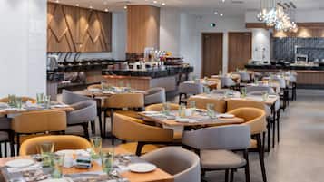 En modern restaurang med flera bord och stolar, en bardisk och ett kök i bakgrunden.