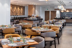 A modern restaurant with multiple dining tables and chairs, a bar area, and a kitchen in the background. - Holiday Inn Sepang Airport (Sepang)