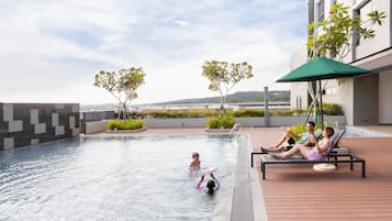En pool med utsikt över havet, ett område med solstolar och parasoller samt en byggnad med modern design.