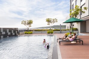 A swimming pool with a view of the sea, a lounge area with umbrellas, and a building with a modern design. - Holiday Inn Sepang Airport (Sepang)