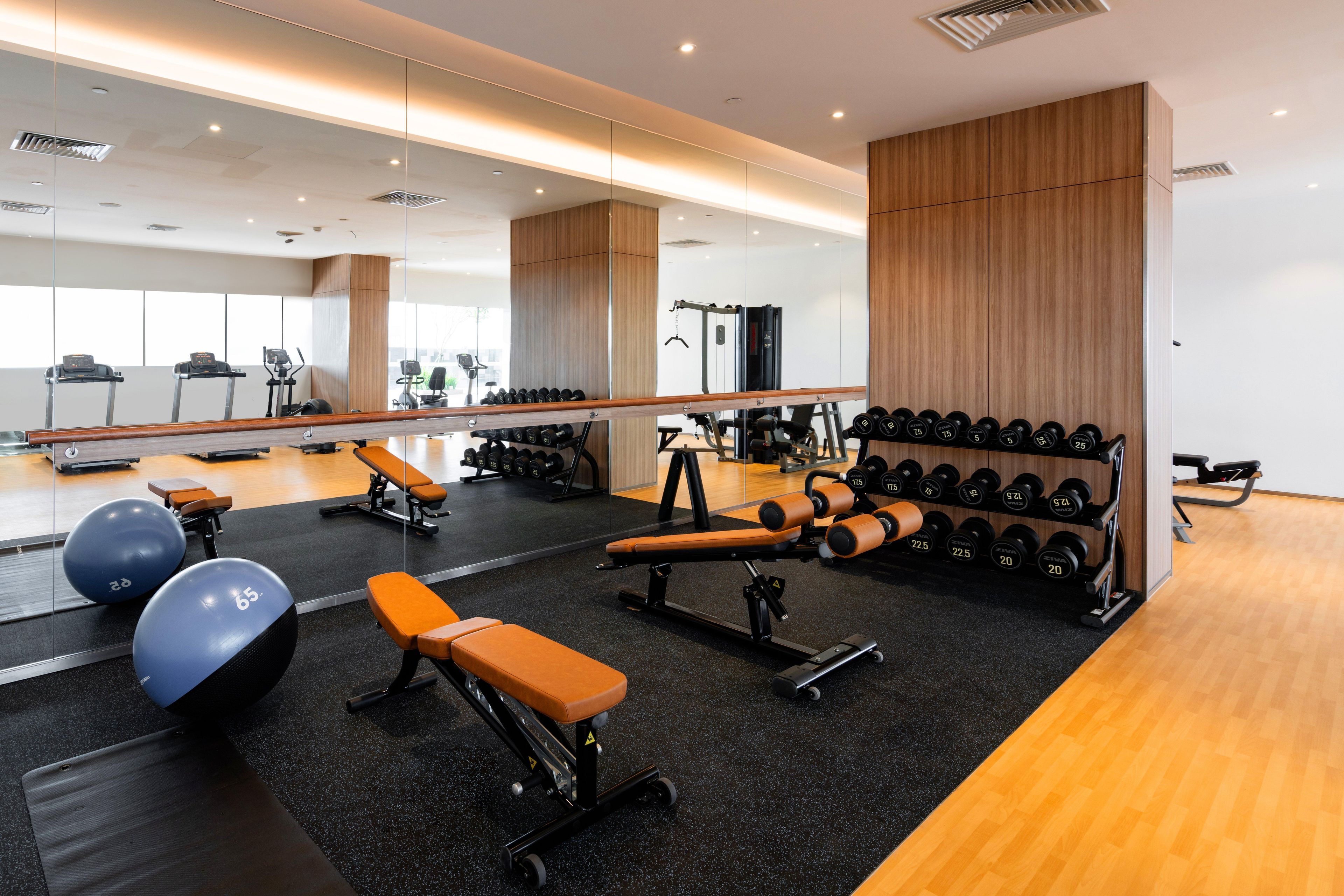 A modern gym with exercise equipment, benches, and a mirrored wall.