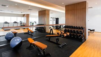 A modern gym with exercise equipment, benches, and a mirrored wall.