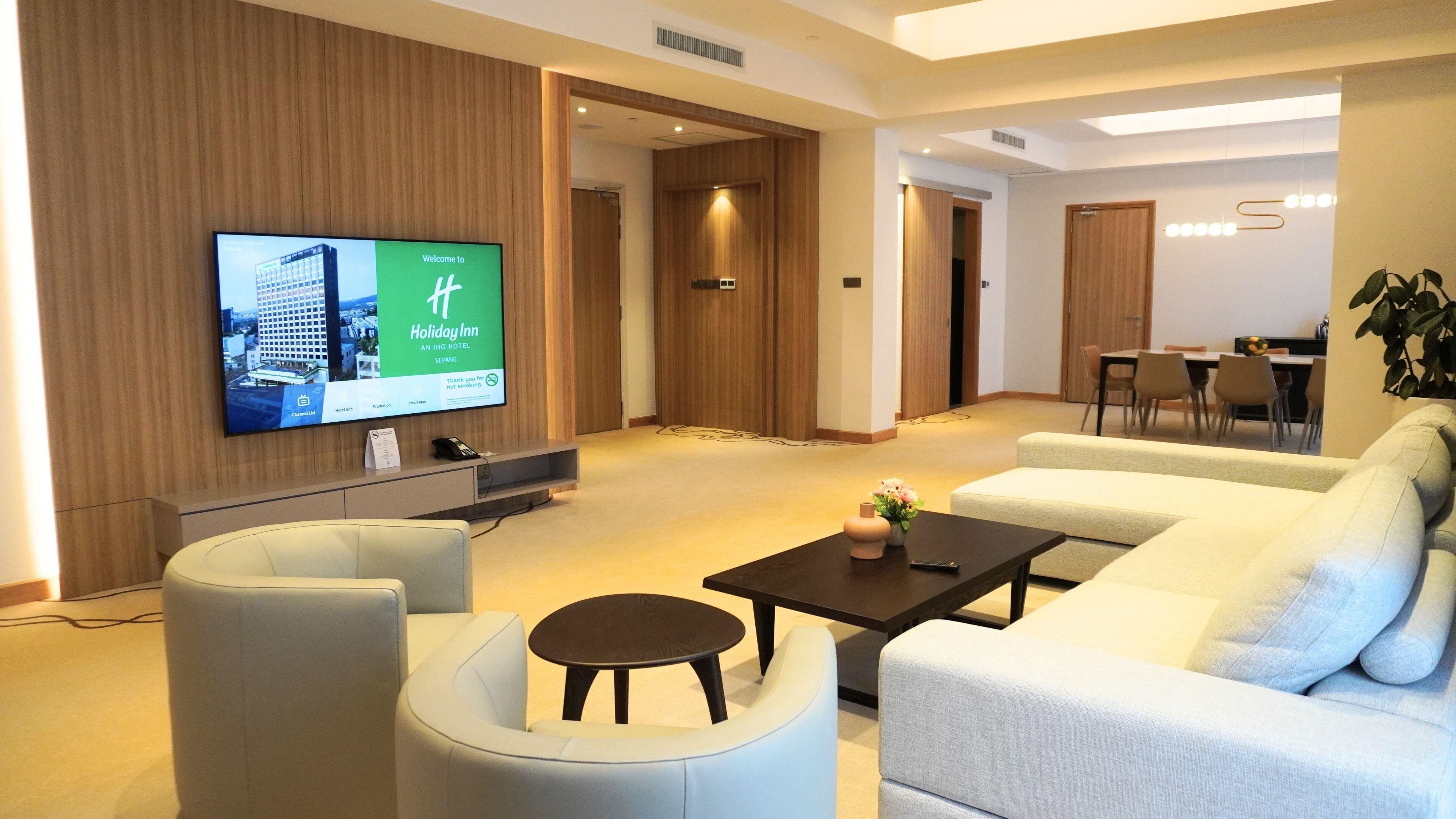 A modern hotel lobby with a flat-screen TV, a sofa, a coffee table, and a dining area.