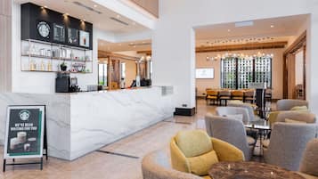 A modern hotel lobby with a marble reception desk, seating area, and a large screen displaying a presentation.