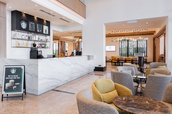 A modern hotel lobby with a marble reception desk, seating area, and a large screen displaying a presentation. - Holiday Inn Sepang Airport (Sepang)