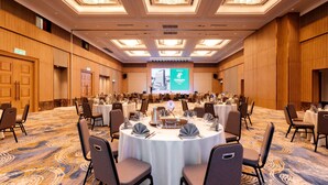 A conference room with round tables, chairs, and a large screen displaying a presentation. - Holiday Inn Sepang Airport (Sepang)