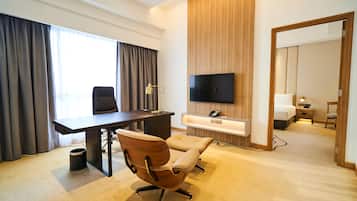 A hotel room with a desk, two chairs, a TV, a bedside table, and a bed.