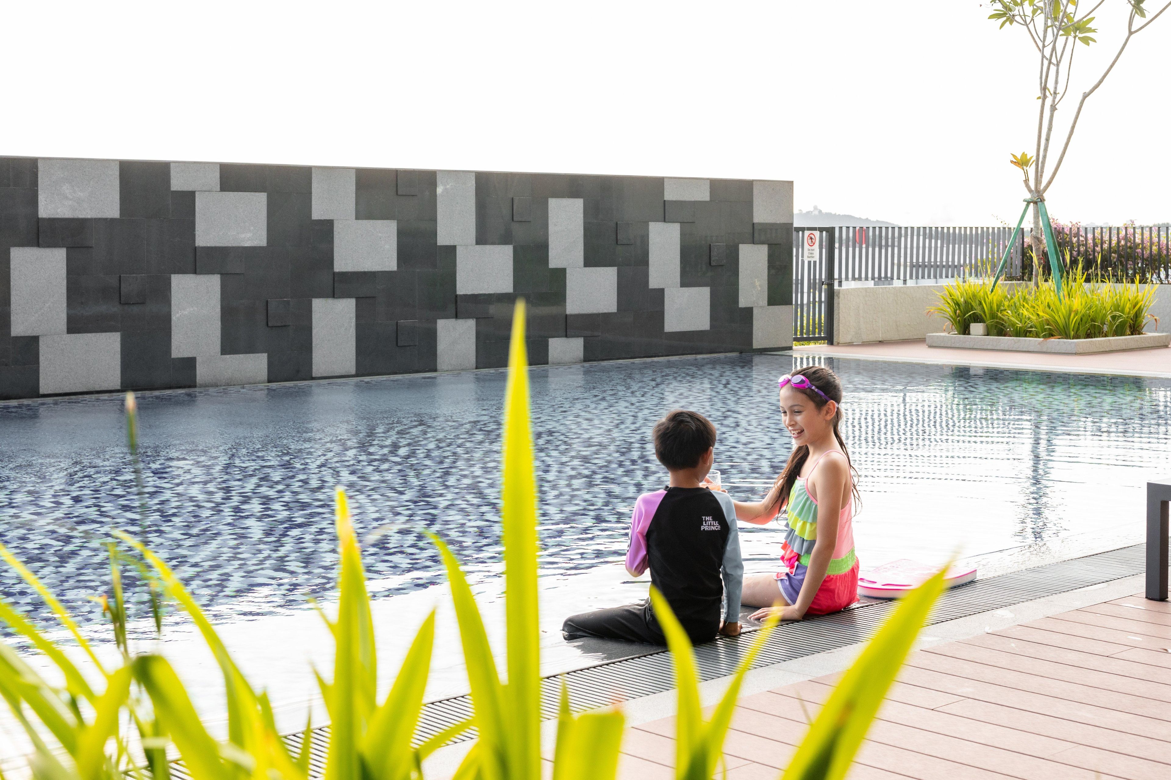 A swimming pool with a modern tiled wall, a wooden deck, and some greenery.