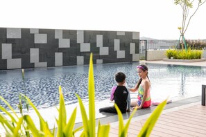 A swimming pool with a modern tiled wall, a wooden deck, and some greenery. - Holiday Inn Sepang Airport (Sepang)
