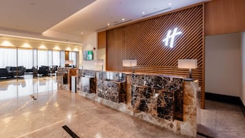 A modern reception desk with a marble top, wooden paneling, and a large illuminated sign.