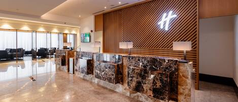 A modern reception desk with a marble top, wooden paneling, and a large illuminated sign.