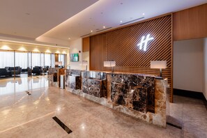 A modern reception desk with a marble top, wooden paneling, and a large illuminated sign. - Holiday Inn Sepang Airport (Sepang)