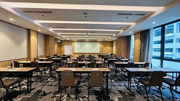 Una sala de conferencias con una pantalla grande, varias mesas y sillas dispuestas para reuniones.