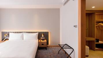 A hotel room with a large bed, bedside table with a lamp, a small table with a lamp, and a wooden closet.