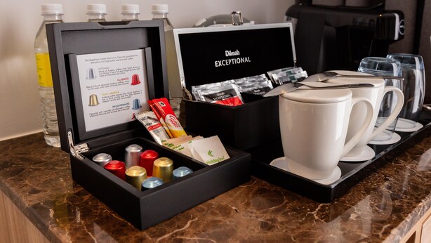 A coffee station with a coffee maker, cups, and a box containing coffee capsules and a bottle of water. - Holiday Inn Sepang Airport (Sepang)