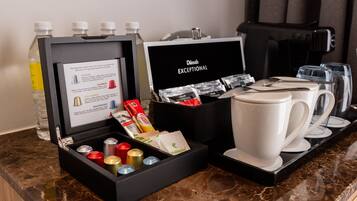 A coffee station with a coffee maker, cups, and a box containing coffee capsules and a bottle of water.