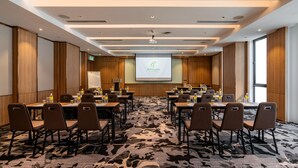 A conference room with a large screen displaying 'Holiday Inn' branding, multiple tables with chairs, and a carpeted floor. - Holiday Inn Sepang Airport (Sepang)
