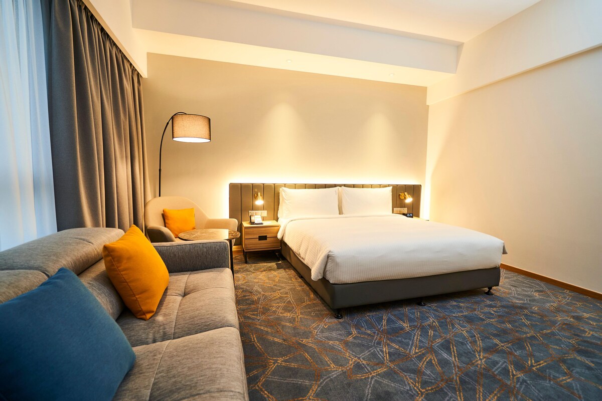 A hotel room with a bed, a sofa, a nightstand, and a lamp.