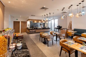 A modern dining area with a buffet, seating arrangements, and a kitchen in the background. - Holiday Inn Sepang Airport (Sepang)