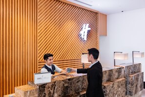 A reception desk with a wooden panel wall, a marble counter, and a sign reading 'IHG ONE REWARDS'. - Holiday Inn Sepang Airport (Sepang)