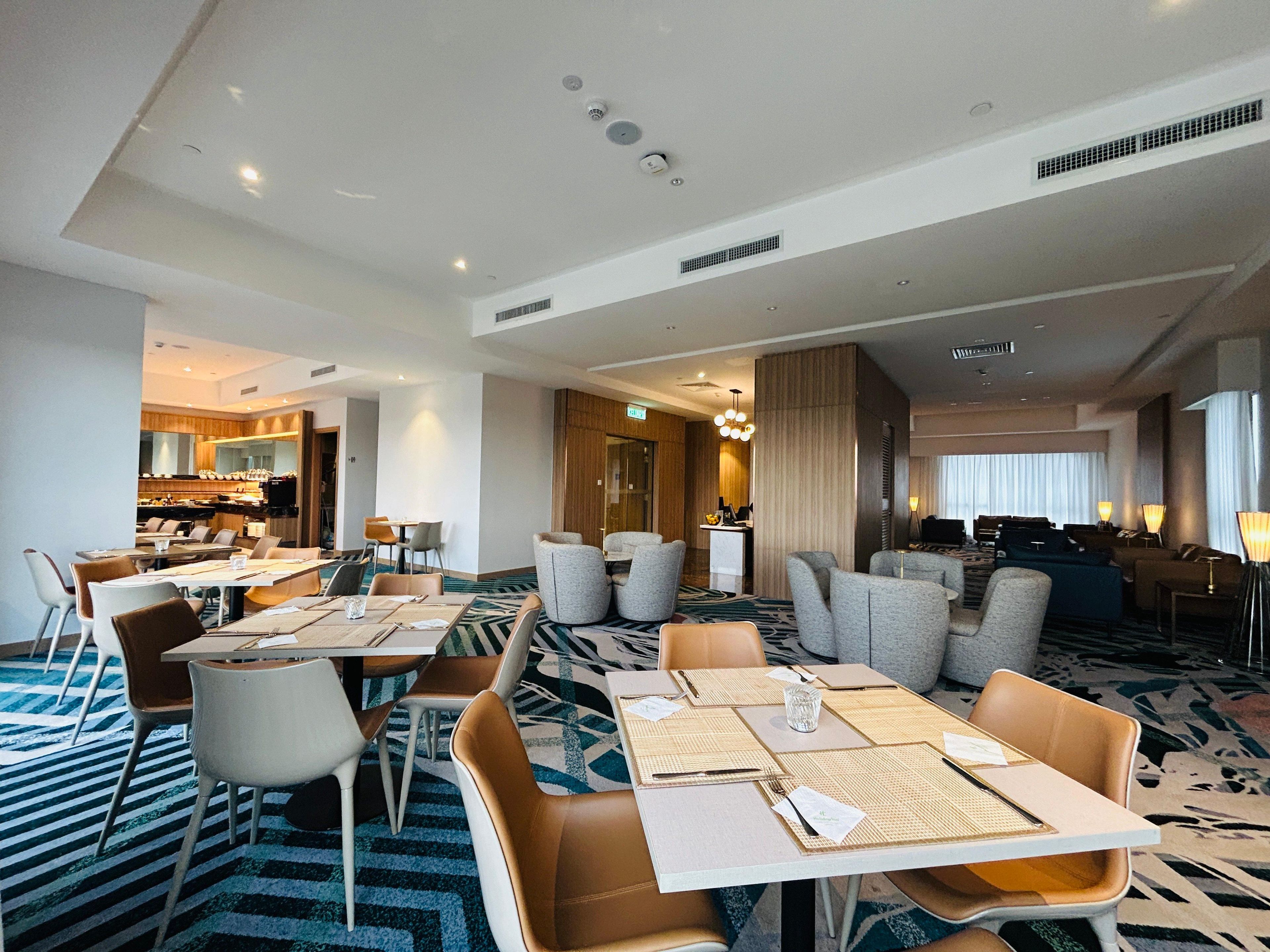 A hotel dining area with tables, chairs, and a kitchen in the background.