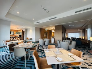 A hotel dining area with tables, chairs, and a kitchen in the background. - Holiday Inn Sepang Airport (Sepang)