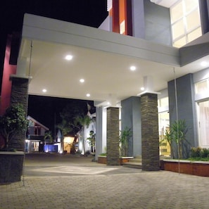 Un edificio moderno con un acceso cubierto, pilares de piedra y un camino pavimentado.