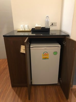 A compact kitchenette with a refrigerator, a small countertop, and a cabinet. - Hotel IYA (Khlong Luang)