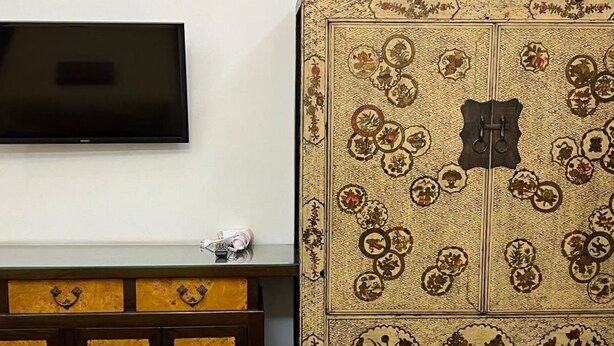 A room with a television mounted on the wall, a wooden cabinet with a patterned design, and a large decorative cabinet with circular motifs. - Hotel IYA (Khlong Luang)