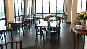 A spacious dining area with multiple tables and chairs, large windows, and chandeliers. - Hotel IYA (Khlong Luang)