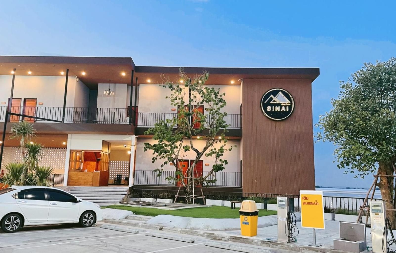 A modern hotel with a sign reading 'SINAI,' a car parked in front, and a charging station.