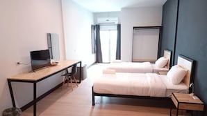 Une chambre d’hôtel moderne équipée d’un bureau en bois, d’une télévision, de deux lits avec des têtes de lit et d’un appareil de climatisation.