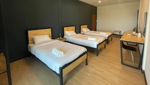 Une chambre d’hôtel avec trois lits simples, un bureau en bois, une chaise et une petite table.