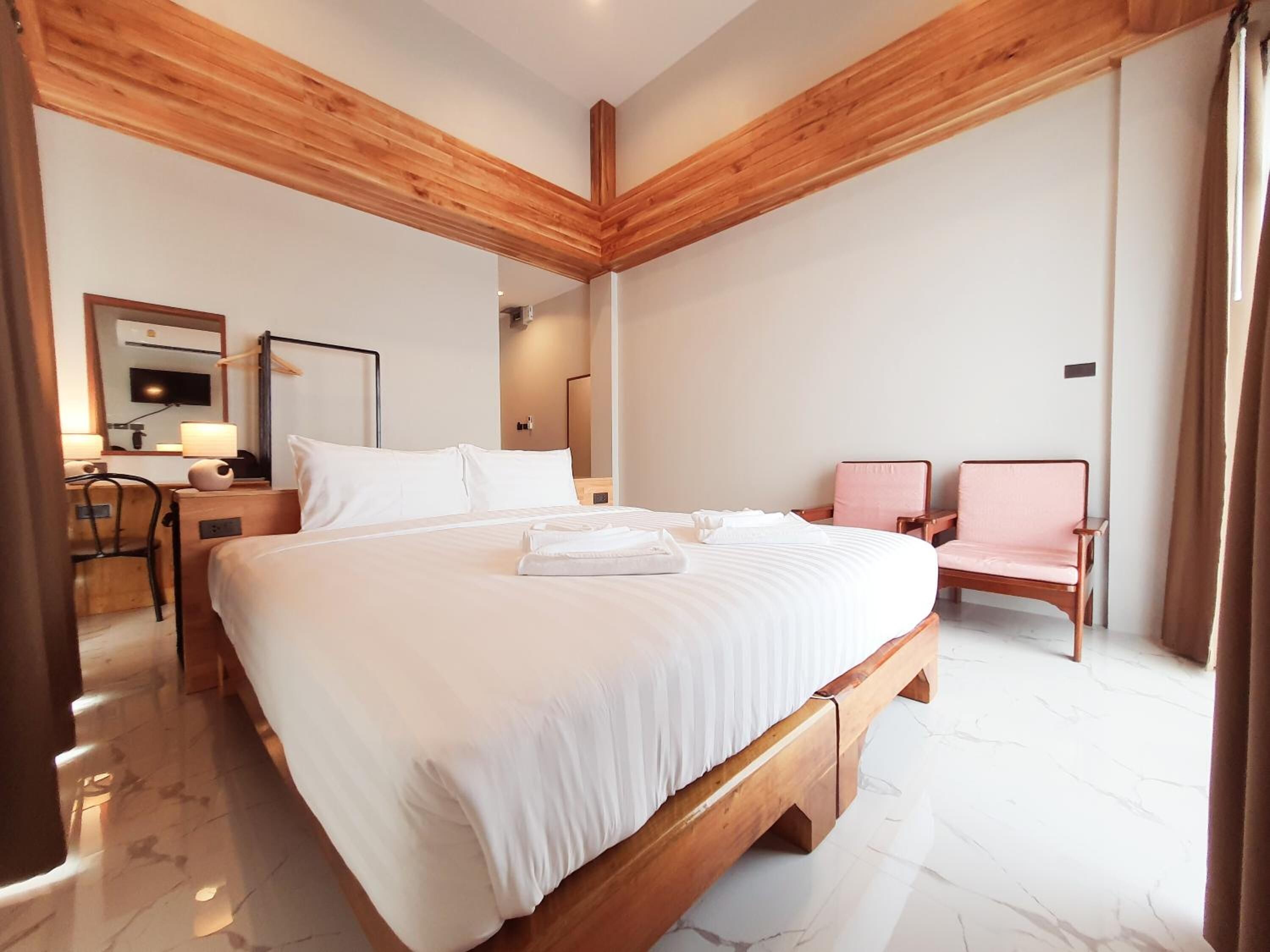 A hotel room with a large bed, a desk with a chair, a small table with a lamp, and two armchairs.