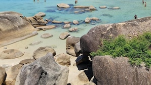 A beach with clear water, rocks, and a forested hillside. - Suhotel Suratthani (Surat Thani)