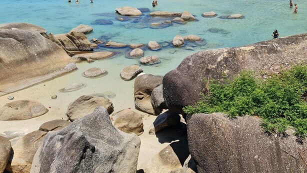 A beach with clear water, rocks, and a forested hillside. - Suhotel Suratthani (Surat Thani)