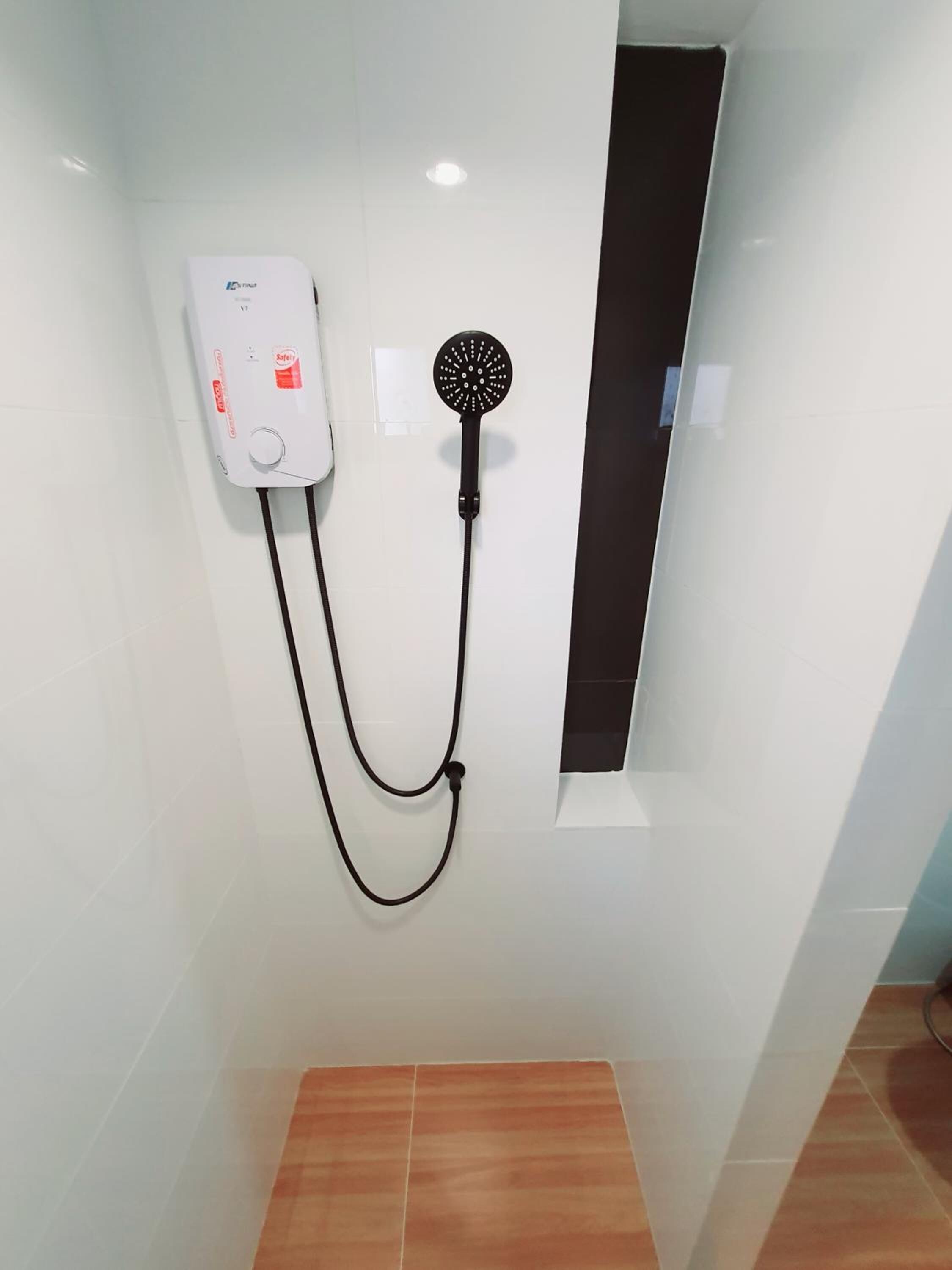 A bathroom with a white wall, a showerhead, and a white water heater.