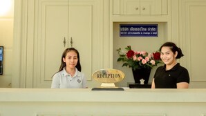 A reception desk with a 'RECEPTION' sign, a framed notice, and a vase of flowers. - Ivory Palace Hotel (Pattaya)