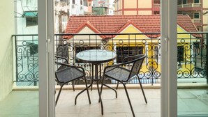 A balcony with a table and chairs, a view of buildings with red roofs, and a large air conditioning unit. - Ivory Palace Hotel (Pattaya)