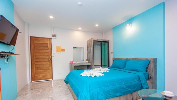 Un dormitorio con cama, puerta de madera, espejo, armario, televisor y mesa de vidrio.